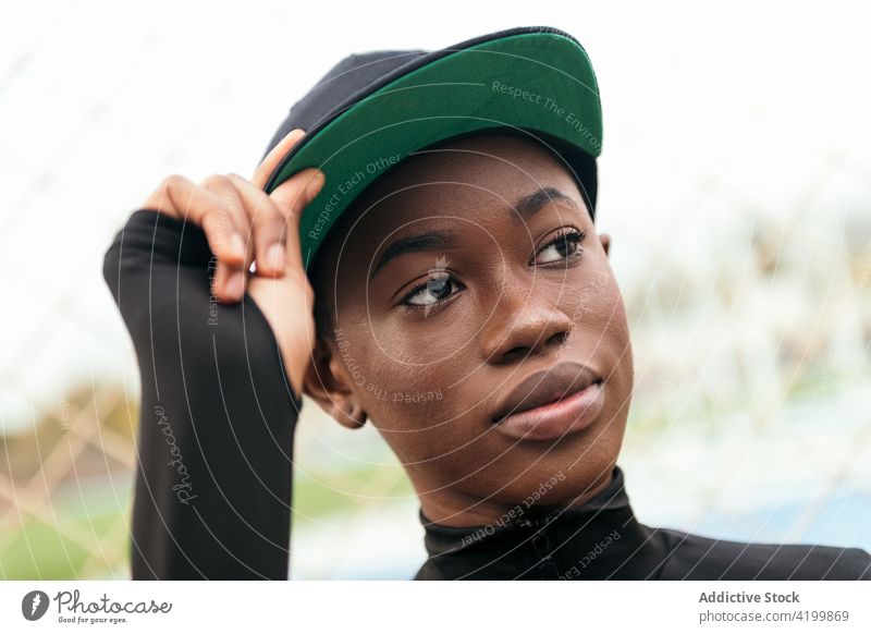 Cool black woman in cap against grid fence individuality cool style finger up trendy city portrait wear casual garment gentle modern cloth african american