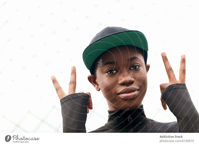 Cool black woman in cap against grid fence individuality cool style finger up trendy city portrait wear casual garment gentle modern cloth african american