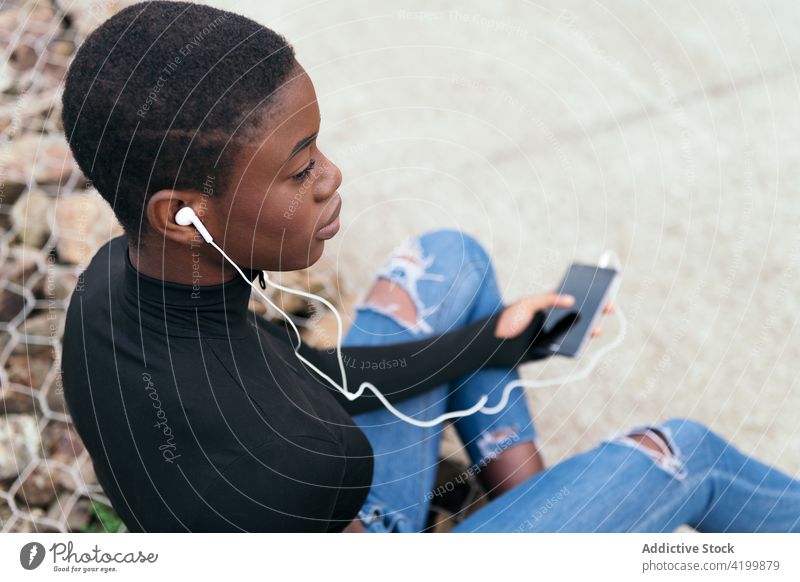 Short-haired black woman listening to music with a mobile phone and headphones african american smartphone headset song short hair portrait using gadget town