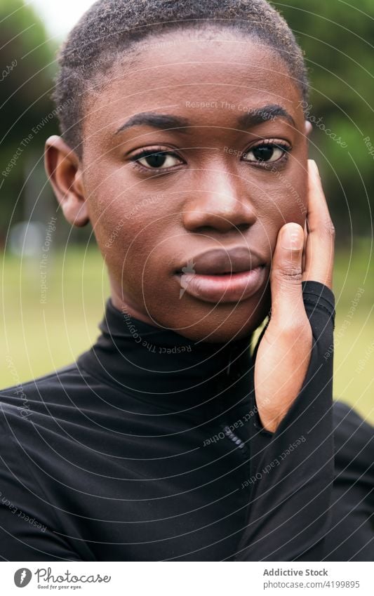 Gentle black woman in casual wear in city park feminine gentle short hair tender sincere friendly charming pleasant portrait urban lawn body belly harmony style