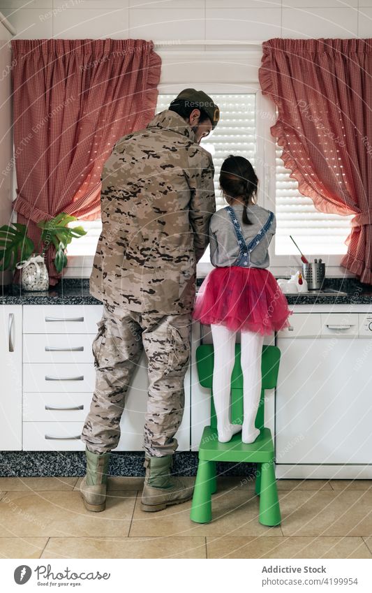 Military man standing at counter with daughter in kitchen military father together soldier home serviceman wash homecoming arrive love child male kid girl house