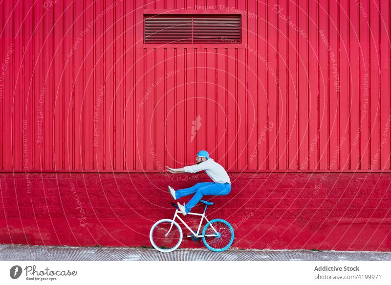 Hipster man jumping near bicycle on city street ride bike cyclist active trick trendy building male beard outfit cap hipster style urban modern transport