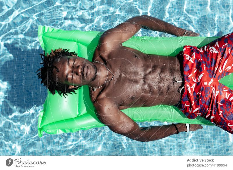 Black man relaxing on inflatable mattress in pool carefree summer vacation enjoy smile male ethnic black african american shorts lying naked torso shirtless