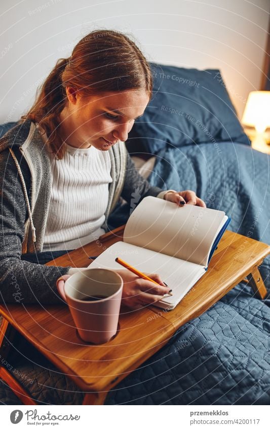 Student learning at home. Young woman making notes, reading and learning from notepad. Girl writing journal sitting in bed education indoor student working