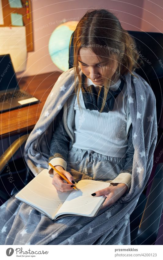 Student learning remotely from home. Young woman having classes online, making notes, reading and learning sitting at desk education indoor student working