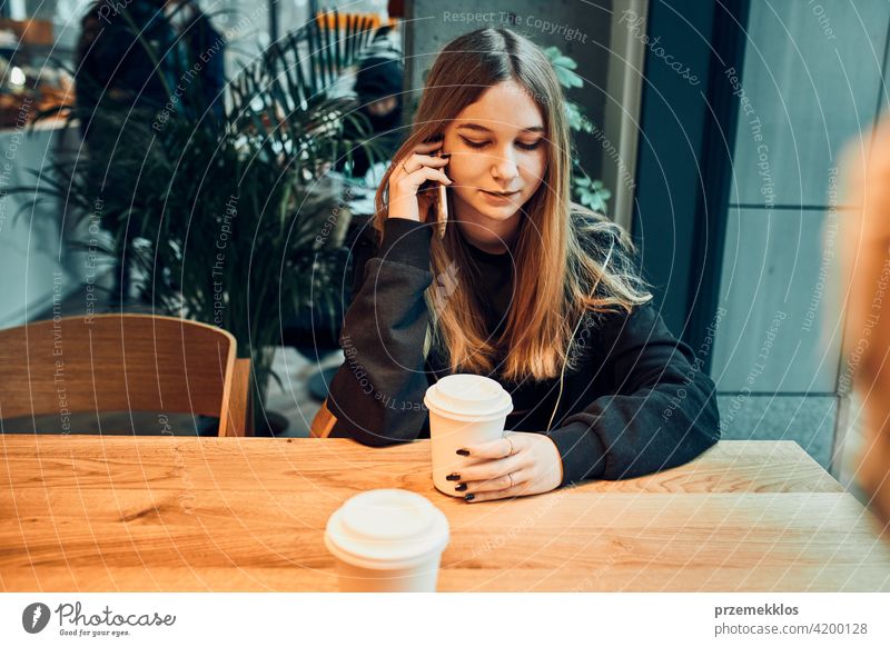 Young woman talking on the phone at cafe, having a pleasant phone call, answering call, chatting by mobile phone with friend while sitting in a cafe and drinking coffee. Girl relaxing in cafe