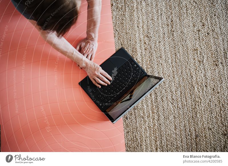 close up view of mature caucasian senior woman practicing yoga pose at home. using laptop for online class with teacher. Healthy and technology lifestyle sport