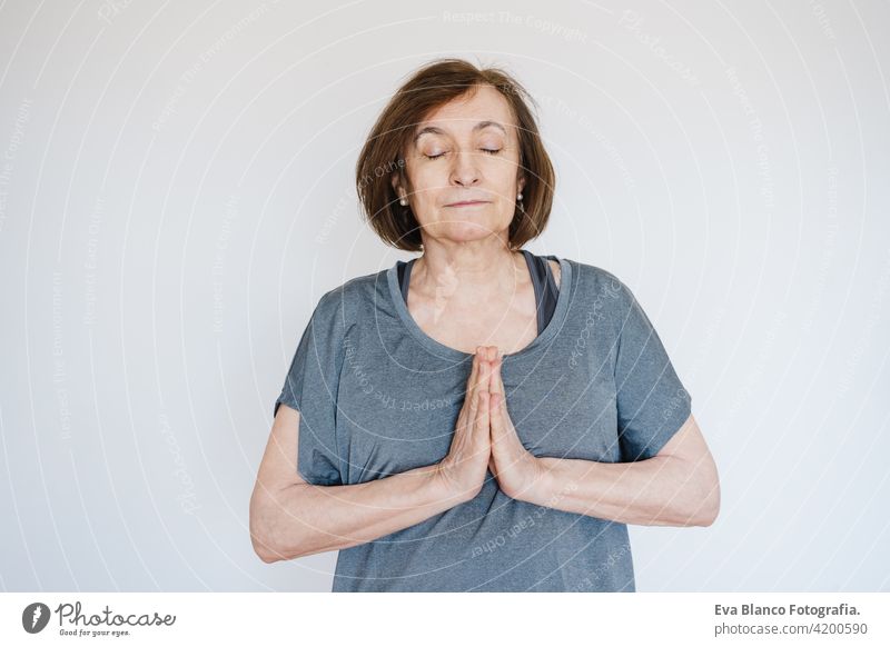 mature caucasian senior woman practicing yoga at home on yoga mat. hands together on praying pose. Healthy lifestyle sport healthy floor old active pensioner