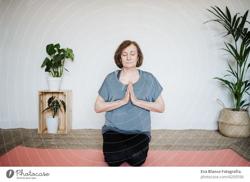 mature caucasian senior woman practicing yoga at home on yoga mat. hands together on praying pose. Healthy lifestyle sport healthy floor old active pensioner