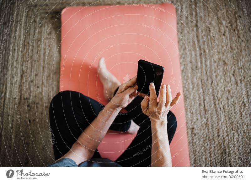 mature caucasian senior woman practicing yoga pose at home. using mobile phone. Technology and Healthy lifestyle technology internet online wireless indoors