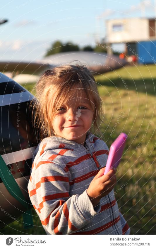 Child plays photographer outdoors. Girl imagines taking pictures on pink plastic toy phone beauty smile lawn hobby concept enjoy shot grass positive fashion