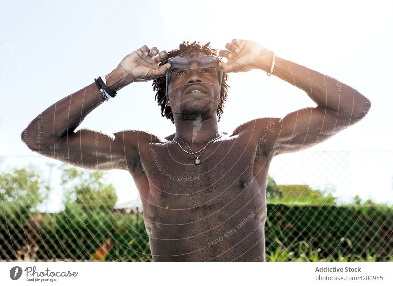 Muscular black guy adjusting swimming goggles after training in outdoor pool man swimmer shirtless muscular athlete poolside confident wellness sportsman