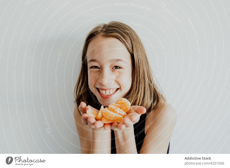 Cheerful girl showing mandarin slices and smiling at camera demonstrate tangerine smile positive portrait fruit vitamin healthy food glad cheerful fresh child