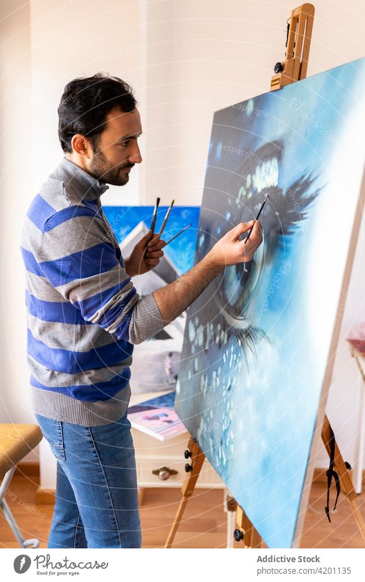 Hispanic male artist painting picture in workshop canvas artwork creative design talent professional man brush painter hispanic ethnic attentive casual wear