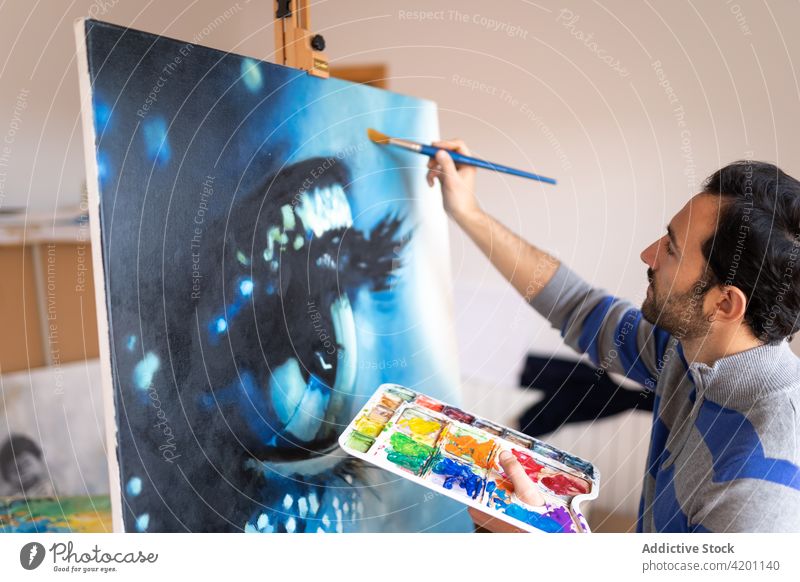 Hispanic male artist painting picture in workshop canvas artwork creative design talent professional man brush painter hispanic ethnic attentive casual wear