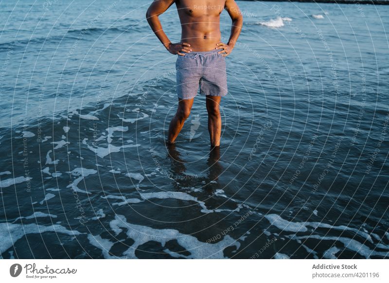 Anonymous black tourist in sea during summer trip ocean vacation hand on waist naked torso travel nature sky man african american foamy wavy seascape endless