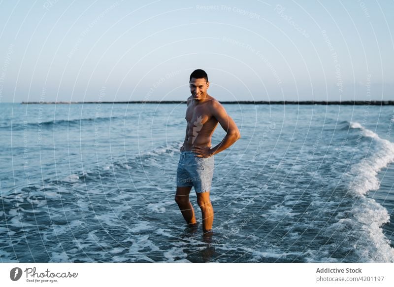 Smiling black tourist in sea during summer trip ocean vacation hand on waist naked torso cheerful travel nature sky man african american foamy wavy seascape