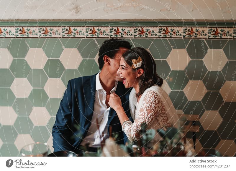 Unrecognizable black groom whispering in ear of smiling bride indoors wedding love vintage relationship celebrate smile decoration restaurant content glad suit