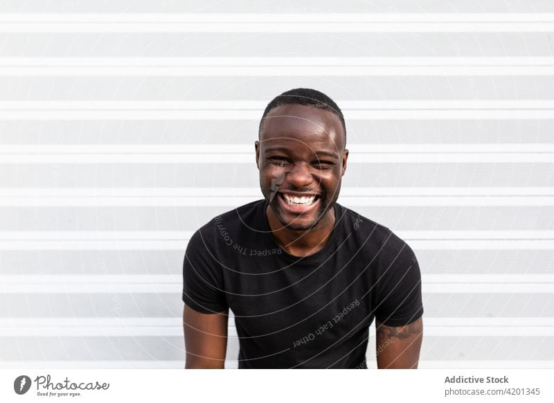 Cheerful black male standing near striped wall man cheerful sincere friendship happy portrait content glad smile candid positive friendly toothy smile enjoy