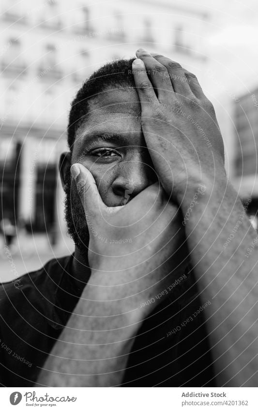 Anonymous African American protester covering face on city street cover mouth cover eye blm movement racial justice equality man portrait town touch head