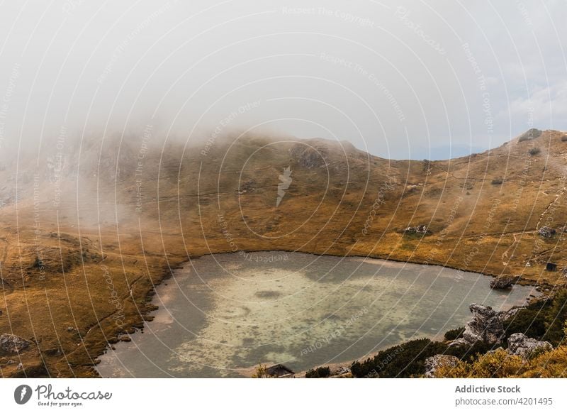 Small lake in foggy highlands mountain hill rock landscape range nature rough dolomites italy water travel tourism ridge picturesque scenic scenery shore