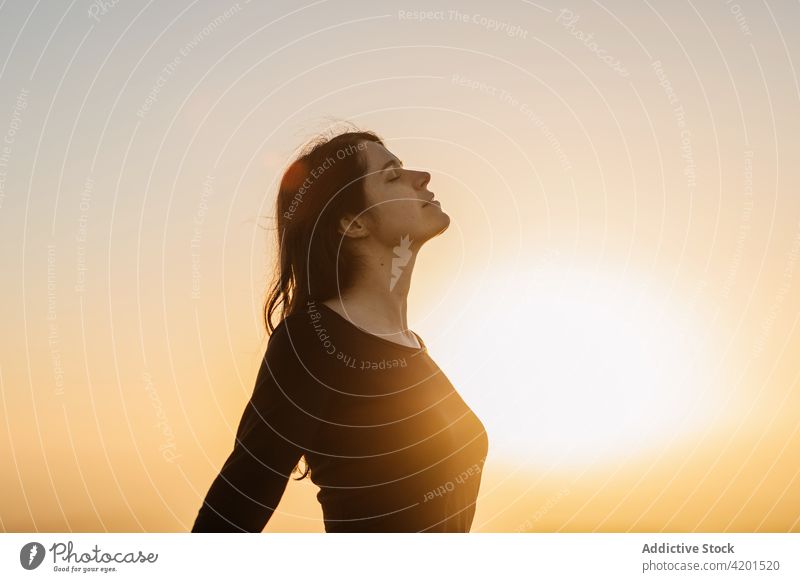 Carefree woman standing on hill and enjoying freedom carefree sunset mountain admire sundown nature female scenery dusk highland idyllic eyes closed twilight