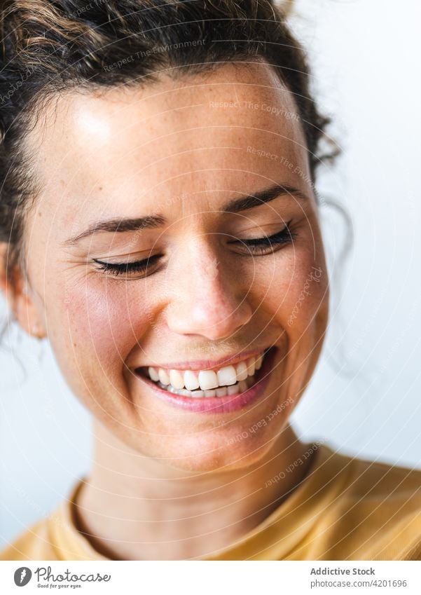 Smiling female with eyes closed against light wall woman positive cheerful smile charming alone optimist glad portrait pleasant toothy smile happy content