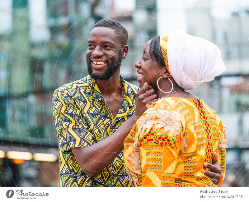 Happy ethnic couple embracing on city street embrace talk relationship love romance soulmate ornament town pavement outfit dress urban building romantic