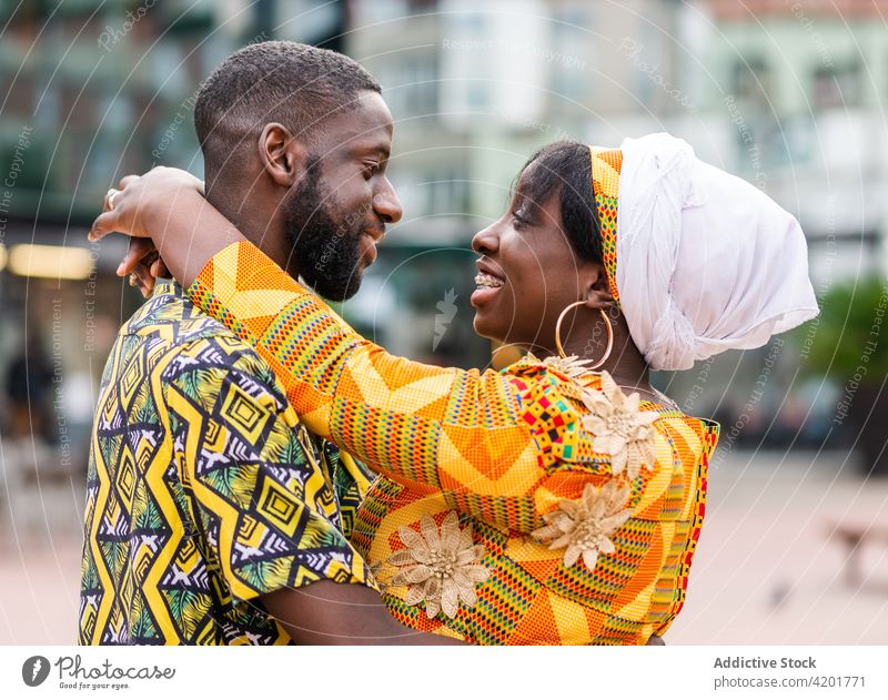 Happy ethnic couple embracing on city street embrace talk relationship love romance soulmate ornament town pavement outfit dress urban building romantic