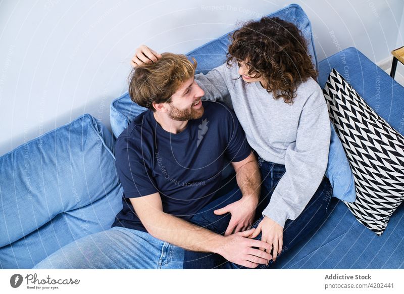 Young couple sitting on sofa and looking at each other happy couch together relationship embrace love hug cheerful romantic smile bonding fondness enjoy relax