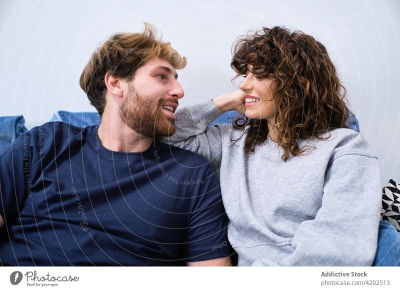 Young couple sitting on sofa and looking at each other happy couch together relationship embrace love hug cheerful romantic smile bonding fondness enjoy relax