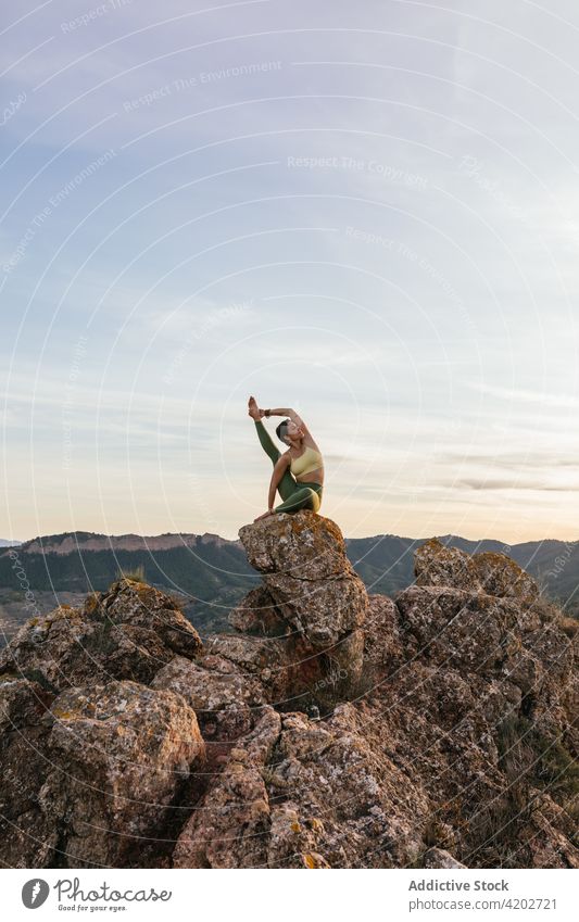 Young woman in Heron posture on mountain yoga cliff heron karuncasana vitality zen practice balance equilibrium female harmony flexible energy tranquil healthy