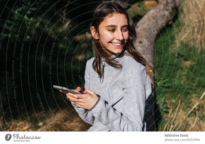 Woman with smartphone resting during hiking in forest woman hiker using mobile active browsing explore nature tree positive young female lifestyle gadget device