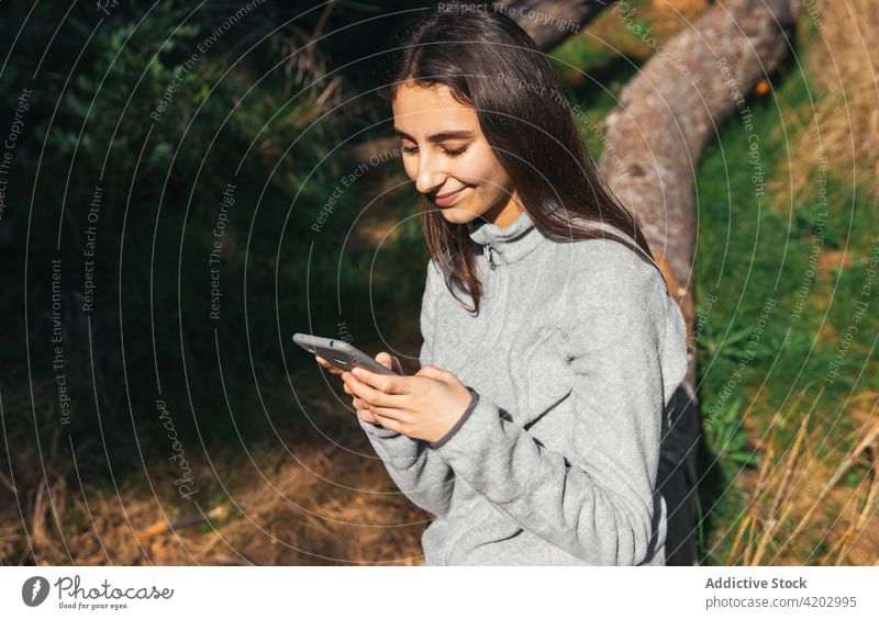 Woman with smartphone resting during hiking in forest woman hiker using mobile active browsing explore nature tree positive young female lifestyle gadget device