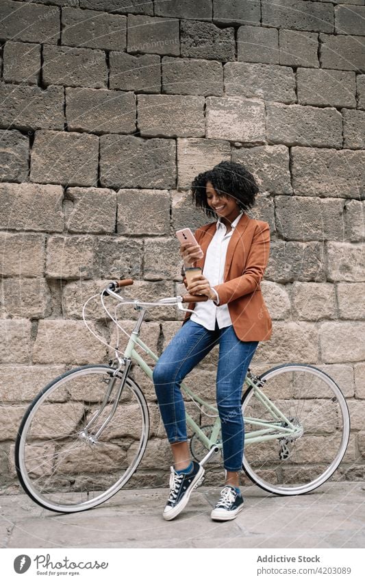 Cheerful black woman browsing smartphone near bicycle in city social media cheerful bike takeaway drink female ethnic african american parked device gadget