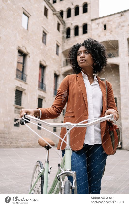 Ethnic woman walking with bicycle along street commute city smart casual bike trendy style female black african american ethnic urban contemporary vehicle town