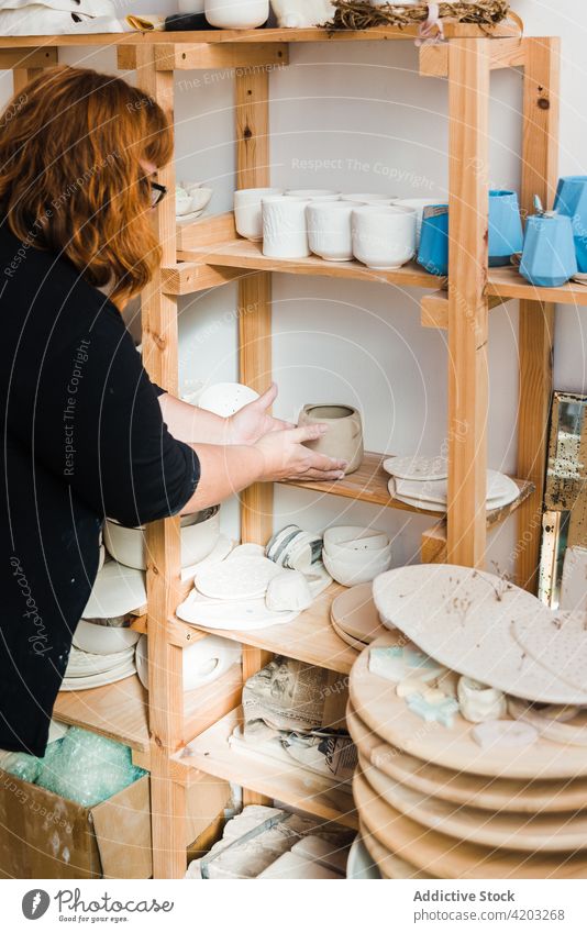 Anonymous female ceramist putting vase on shelf in workshop woman pottery bowl plate earthenware craftswoman handmade casual black various small clay different