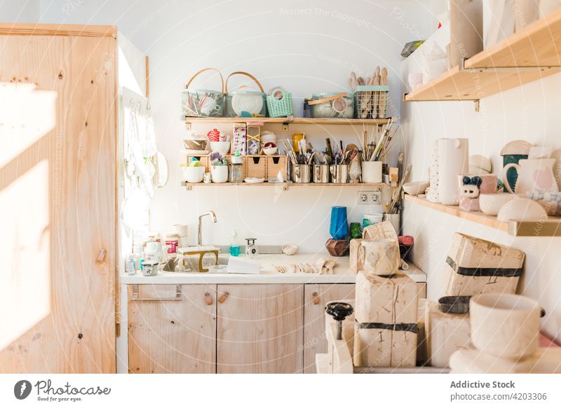 Various tools for pottery on shelves in workshop instrument utensil ceramic small business studio earthenware equipment different wooden shelf sink daylight