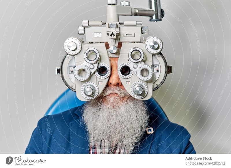 Senior male with phoropter during eye examination optometrist eyesight diagnostic optician ophthalmology optometry examine patient senior doctor vision check