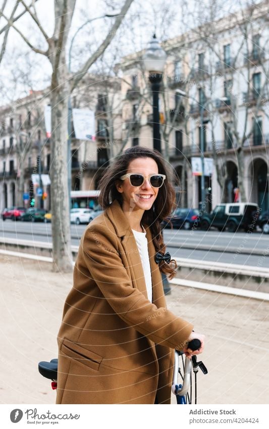 Smiling female biker on bicycle on city street smile weekend spare time woman transport cheerful enjoy vehicle style lifestyle modern pavement coat jeans stand