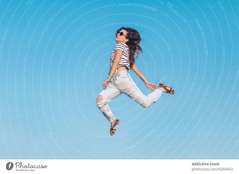 Hipster woman in trendy outfit jumping against blue sky summer style sunglasses fashion carefree hipster stripe energy fly levitate happy casual young female