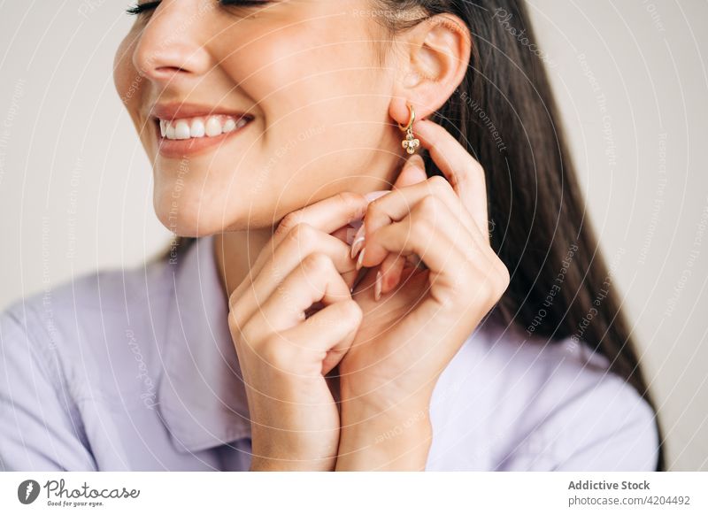 Crop smiling woman touching earring on light background toothy smile eyes closed feminine charming romantic dreamy enjoy portrait accessory creative design