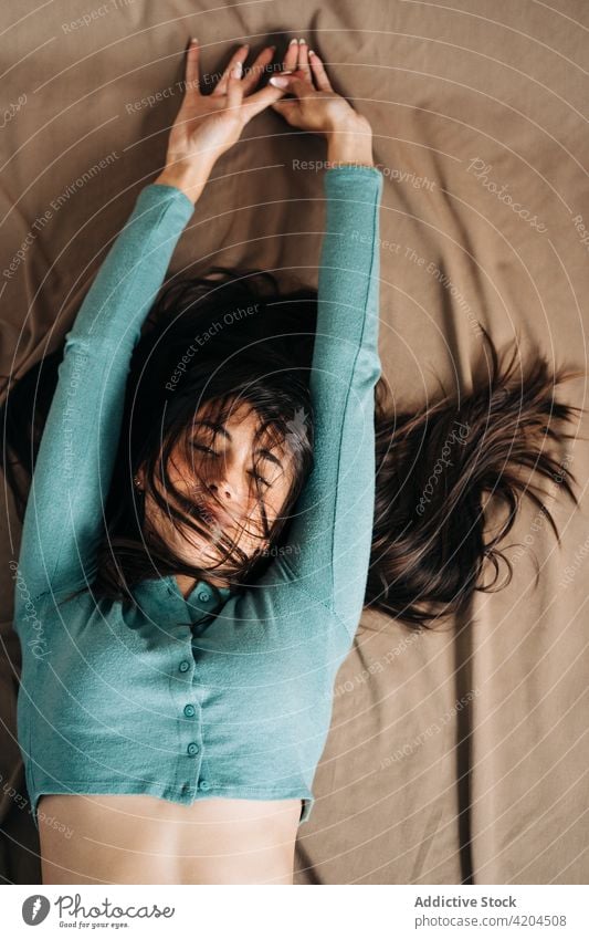 Dreamy woman with raised arms resting on fabric arms raised enjoy mindfulness eyes closed idyllic harmony portrait home domestic crumpled soft house belly