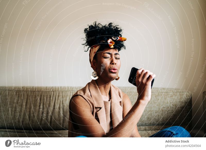 Black woman singing in smartphone at home enjoy song music creative microphone pretend female ethnic black african american favorite sofa weekend eyes closed