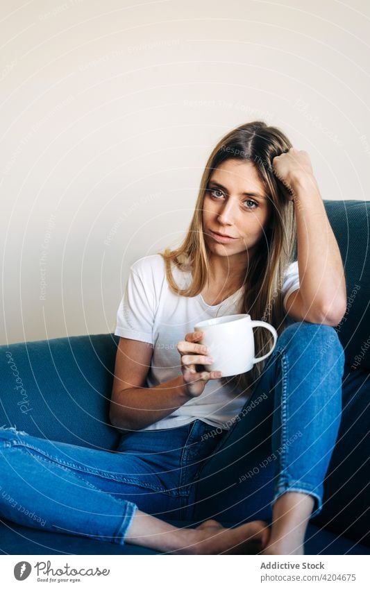 Calm woman with cup on sofa couch drink beverage coffee mug lean on hand leg bent lady female pensive lifestyle relax rest young calm leisure home break