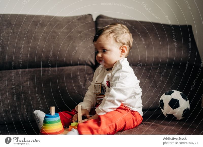 Curious baby playing with toys on couch sofa cone tower playful curious colorful wooden toddler boy child cute childhood babyhood home living room adorable