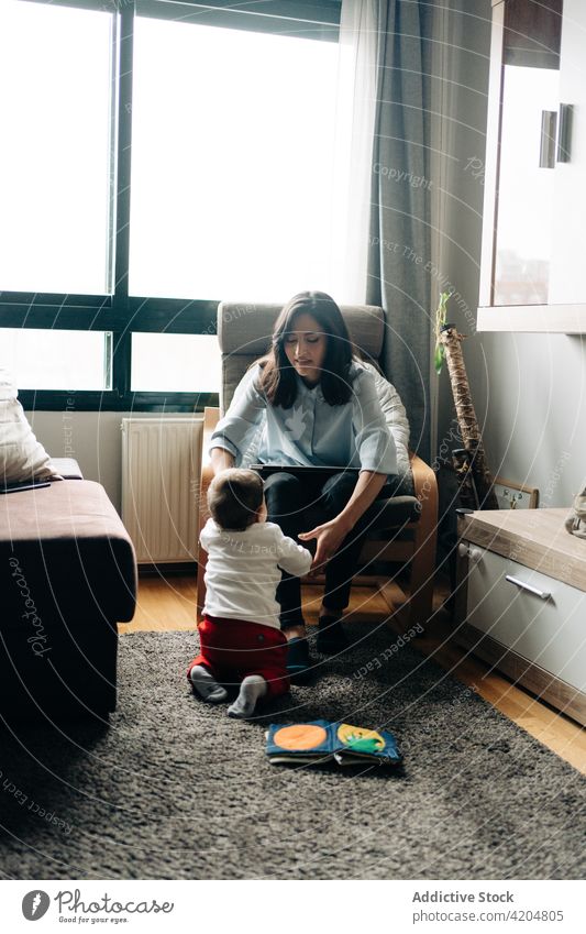 Mother working on laptop near funny little baby mother son smile chair freelance browsing at home parenthood cute woman boy child happy netbook adorable kid