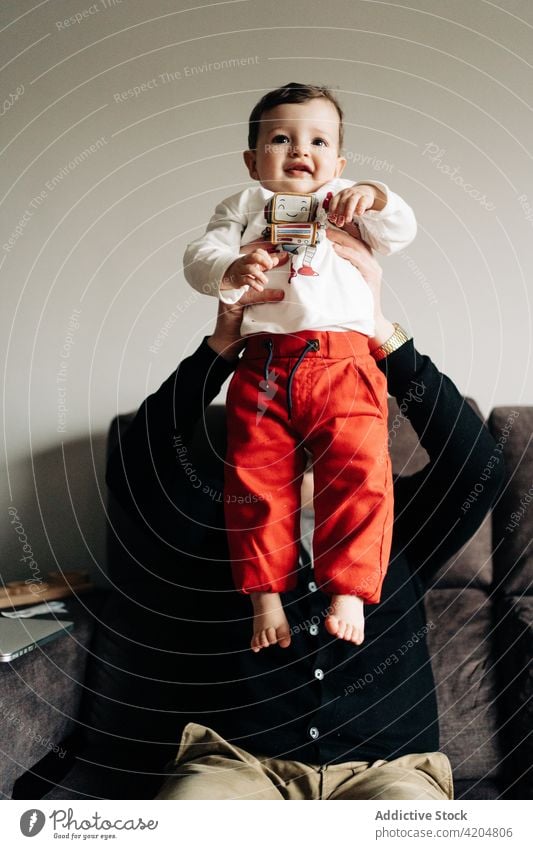 Father lifting little son on hands and sitting on sofa father arms raised together childcare content parenthood cute fondness man fatherhood affection love