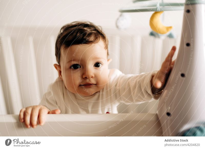 Cute boy standing in crib and playing with shoe gumshoe cute curious interest development childhood cheerful kid innocent playful little adorable toddler sweet