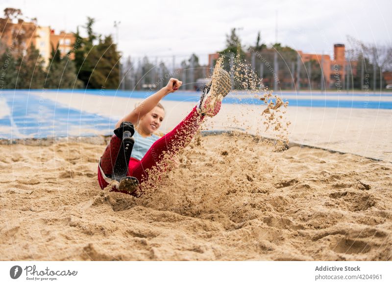 Sportswoman jumping in sandpit during workout at stadium sportswoman prosthesis leg sandbox paralympic athlete training female energy bionic professional